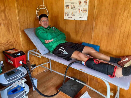 A man lies on a medical bed with a cryotherapy wrap around his lower leg