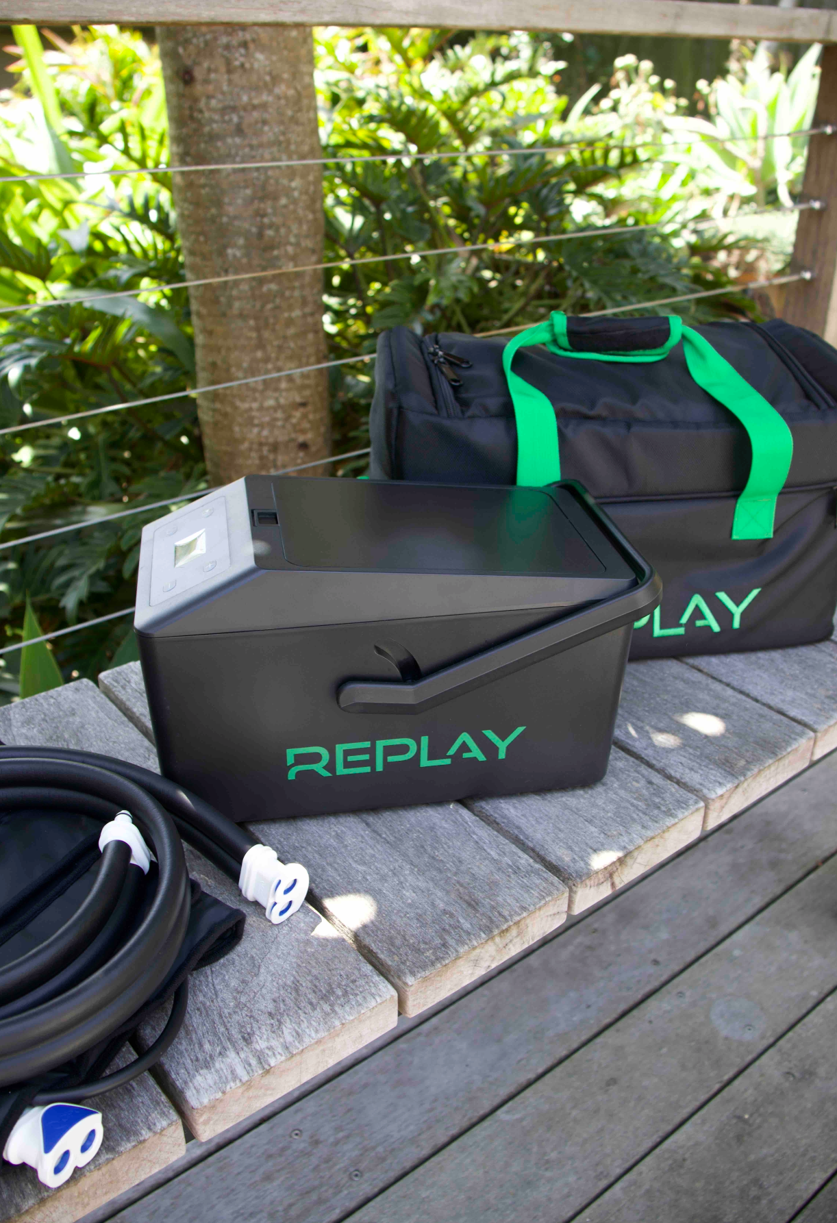 A black bag with the word Replay in green and knee compression pad sit on a wooden bench with plants in the background