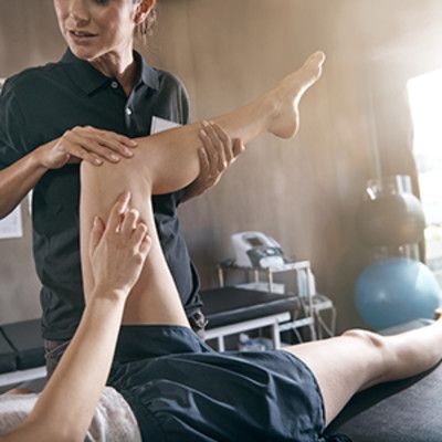 A physio works on a man's knee who is lying down on a physio bed
